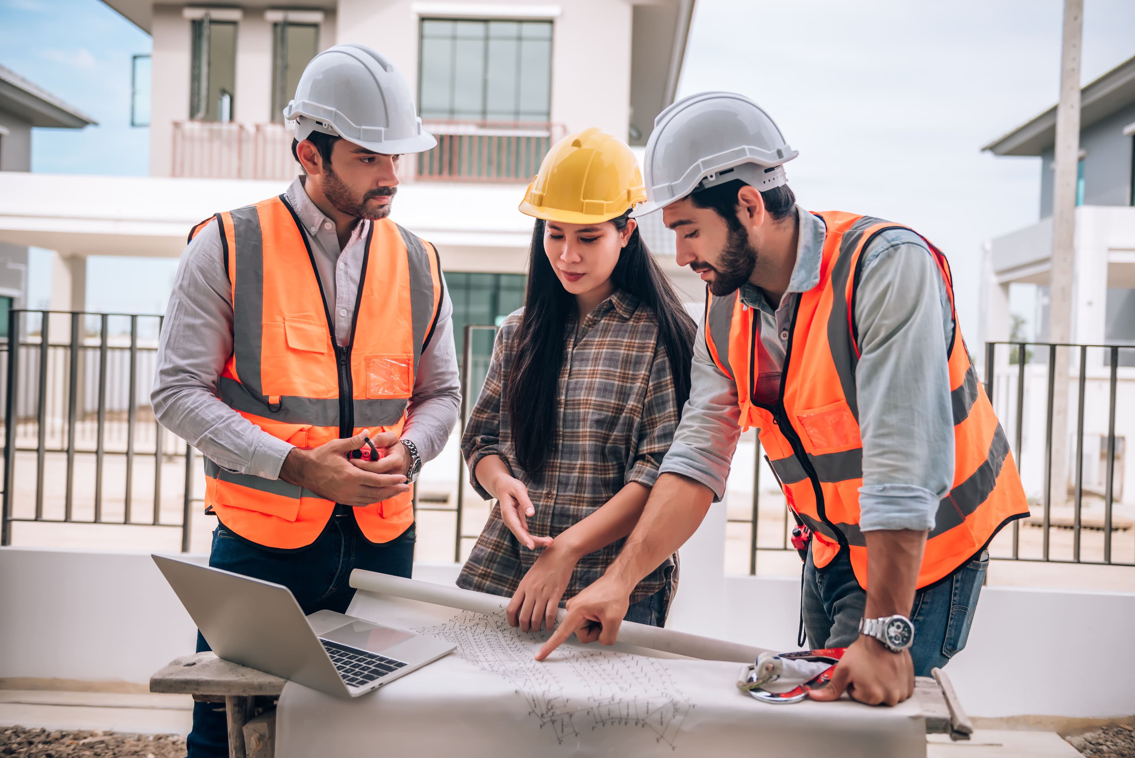 General contracting team in hardhats and safety vests examining site blueprints